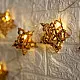 handcrafted banana fiber rope star fairy lights emitting a warm amber glow against a textured white brick wall pattern