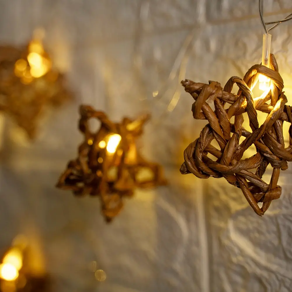 handcrafted banana fiber rope star fairy lights emitting a warm amber glow against a textured white brick wall pattern