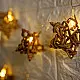 handcrafted banana fiber rope star fairy lights emitting a warm amber glow against a textured white brick wall pattern