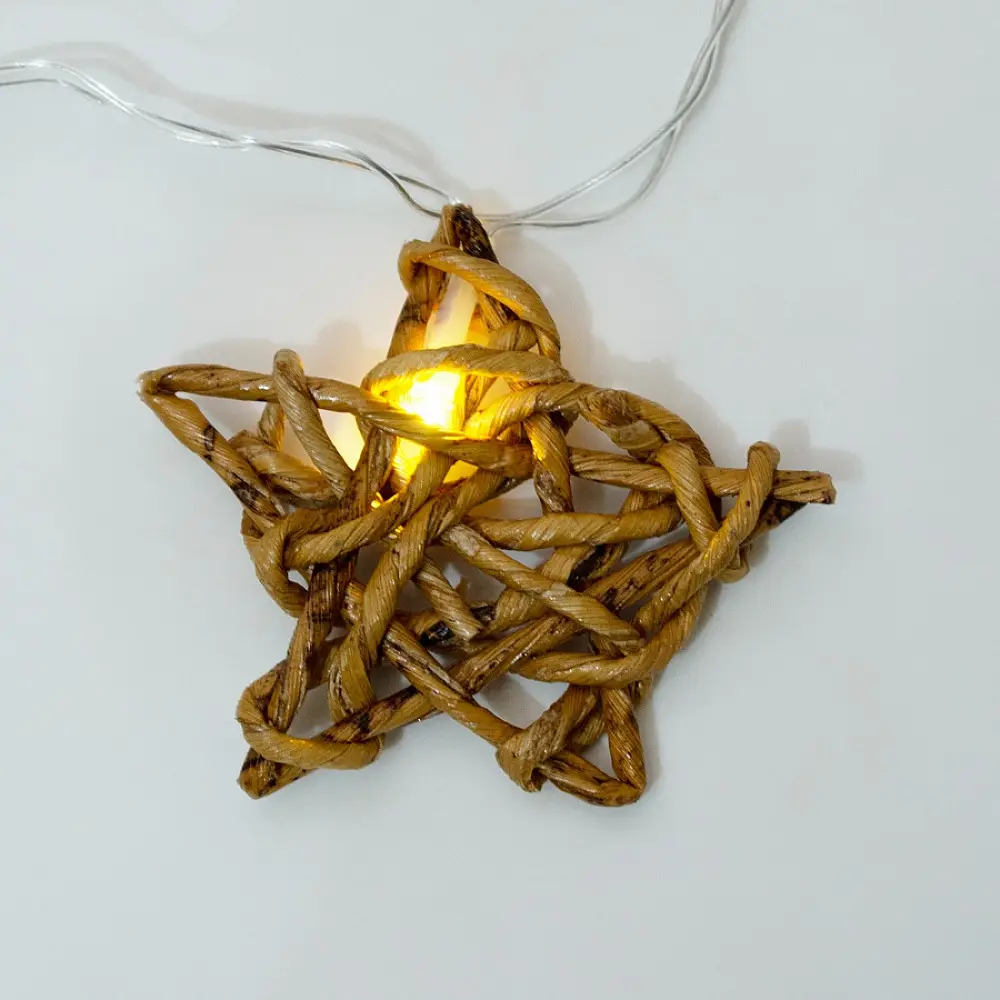 handcrafted banana fiber rope star fairy lights emitting a warm amber glow against a textured white brick wall pattern