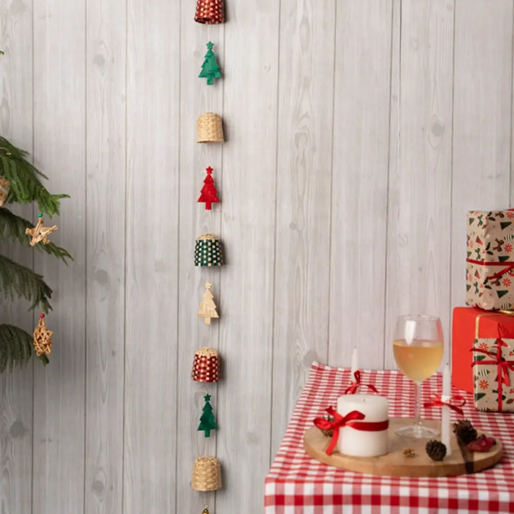 handcrafted vertical christmas string ornament featuring alternating red, green, and checkered bamboo trees and bells against a wooden wall panel