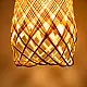 handcrafted woven bamboo twirl pendant light emitting a warm golden glow on a brown background wall