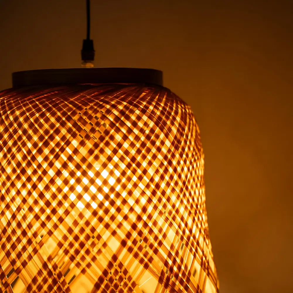 handcrafted woven bamboo twirl pendant light emitting a warm golden glow on a brown background wall