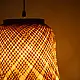 handcrafted woven bamboo twirl pendant light emitting a warm golden glow on a brown background wall