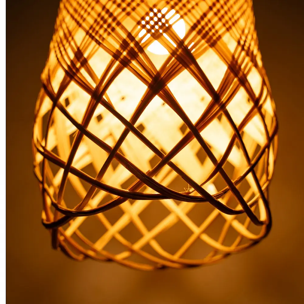 handcrafted woven bamboo twirl pendant light emitting a warm golden glow on a brown background wall