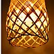 handcrafted woven bamboo twirl pendant light emitting a warm golden glow on a brown background wall
