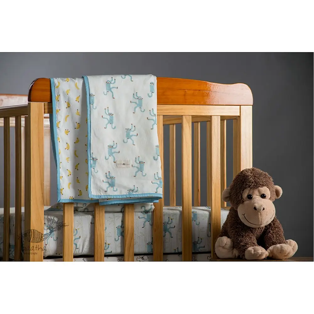 blue fog block printed baby dohar blanket with whimsical monkey and bananas pattern draped over a crib