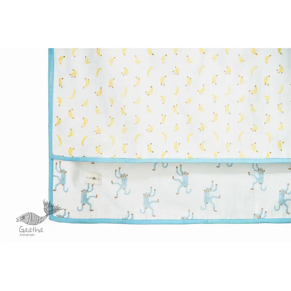 blue fog block printed baby dohar blanket with whimsical monkey and bananas pattern draped over a crib