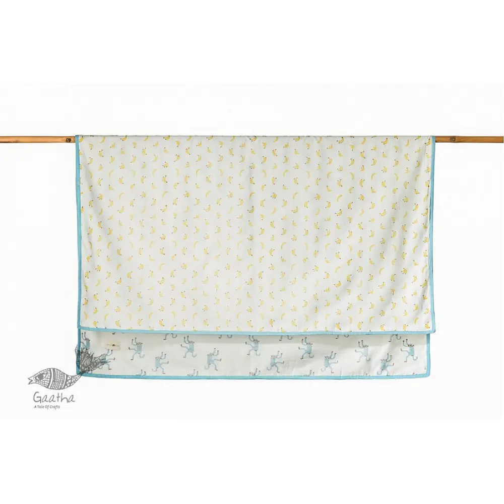 blue fog block printed baby dohar blanket with whimsical monkey and bananas pattern draped over a crib
