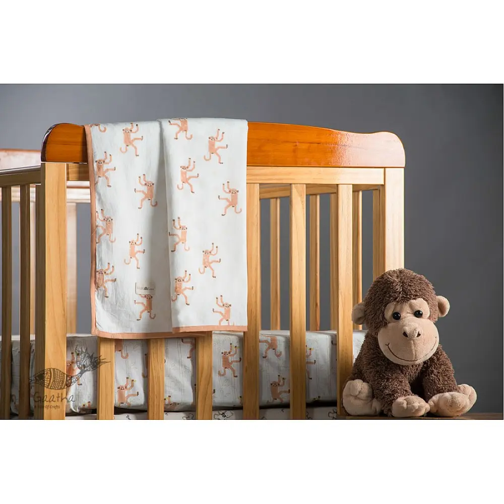 peach apricot block printed baby dohar blanket with whimsical monkey and bananas pattern draped over a crib