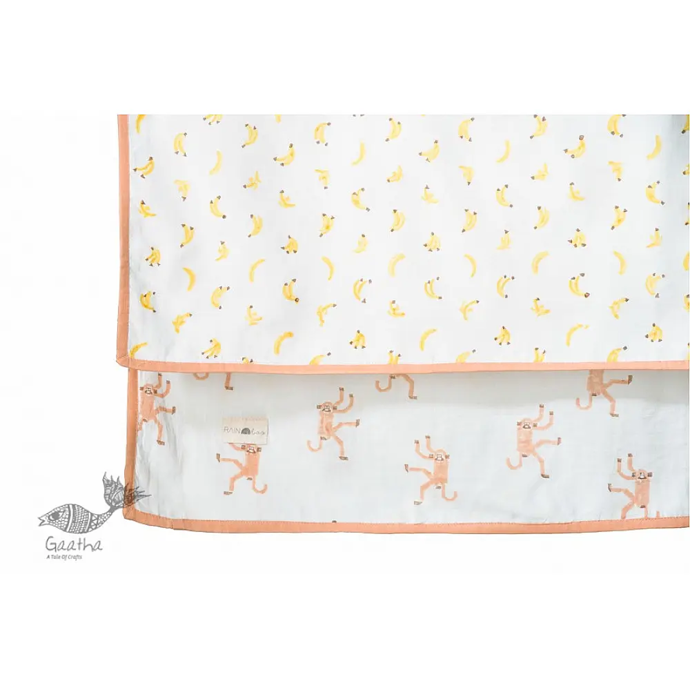 peach apricot block printed baby dohar blanket with whimsical monkey and bananas pattern draped over a crib