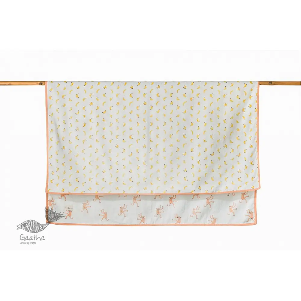peach apricot block printed baby dohar blanket with whimsical monkey and bananas pattern draped over a crib