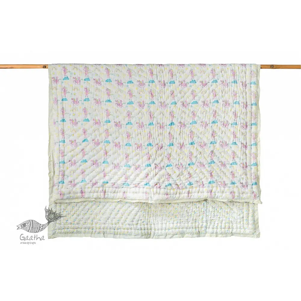mauve and white block printed baby quilt with whimsical unicorns and rainbows pattern draped over a crib