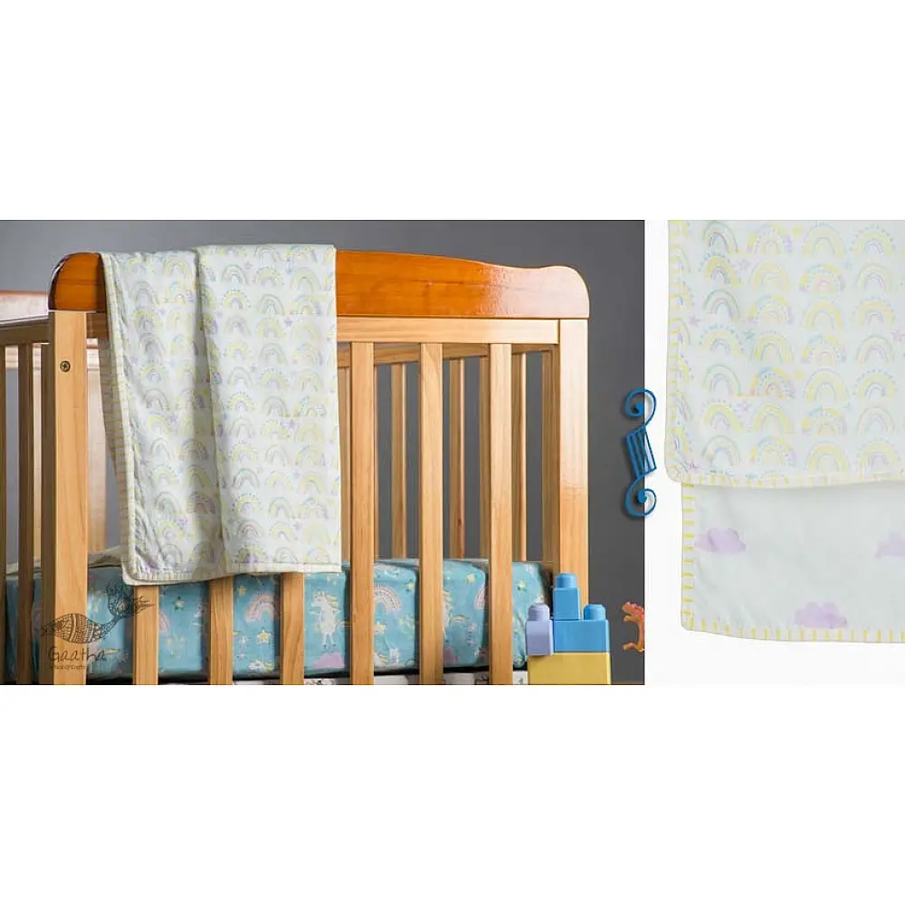 moody mauve block printed baby dohar blanket with whimsical cloud and rainbow pattern draped over a crib