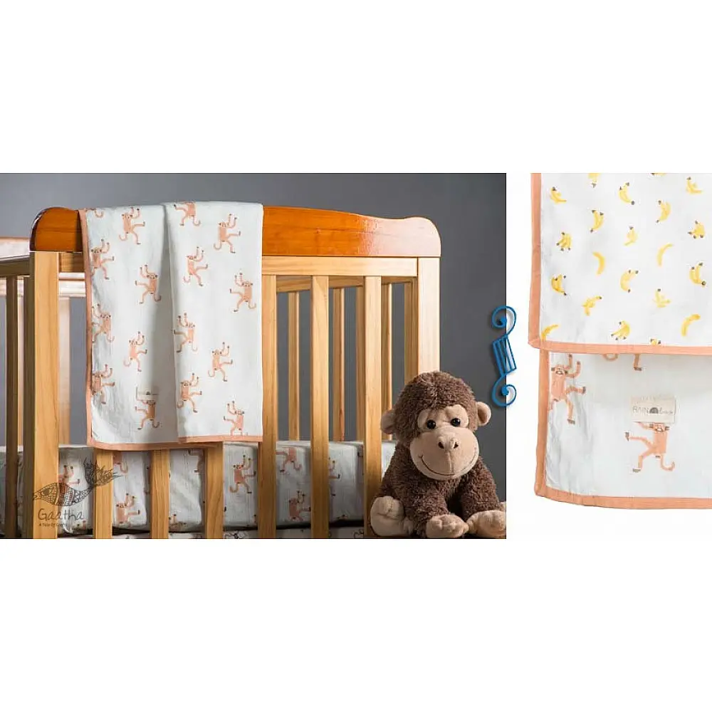 peach apricot block printed baby dohar blanket with whimsical monkey and bananas pattern draped over a crib