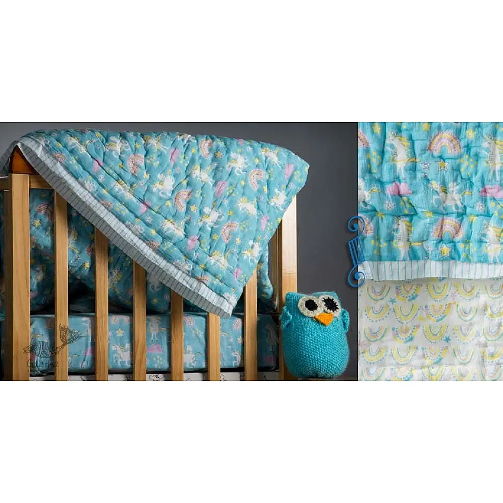 blue and teal block printed baby quilt with whimsical unicorns and rainbows pattern draped over a crib