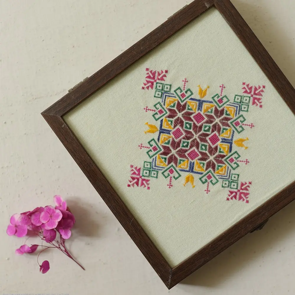 handcrafted square wooden box featuring an ivory fabric top panel with multi-color geometric Soof hand embroidery next to pink flowers