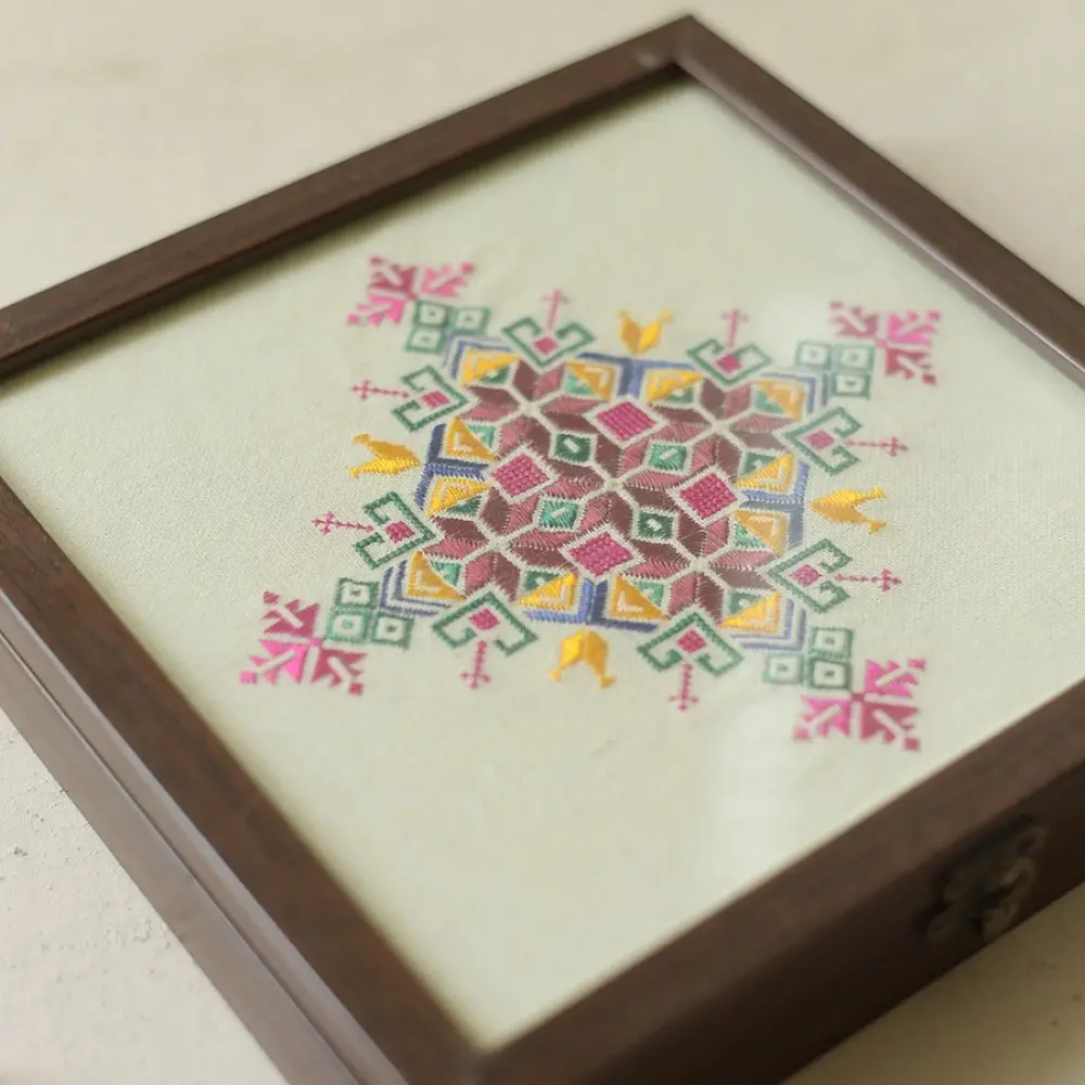 handcrafted square wooden box featuring an ivory fabric top panel with multi-color geometric Soof hand embroidery next to pink flowers